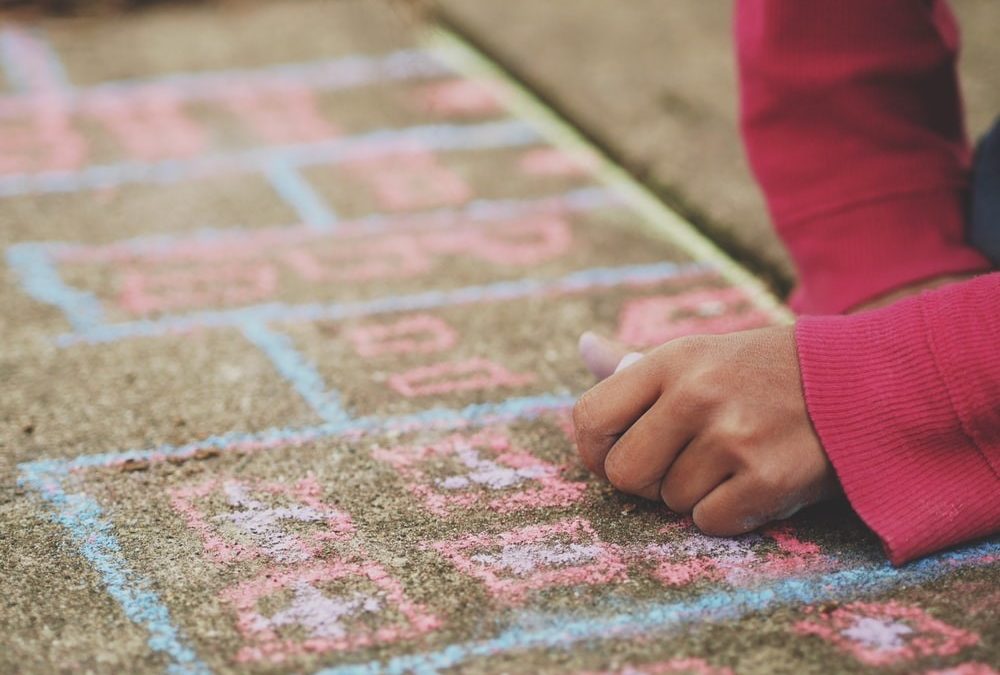 Child using pink and blue chalks to draw on brown carpet.