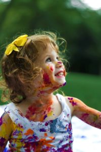 Little girl smiling after painting herself with colors.